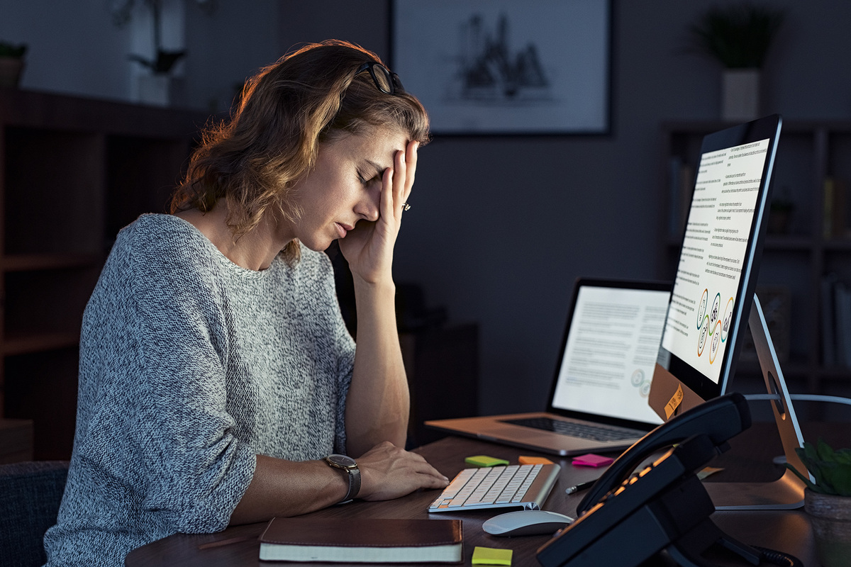 An employee struggles with symptoms of burnout working late hours at her desk.