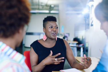 A woman dressed professionally speaks and gestures to other people across a table