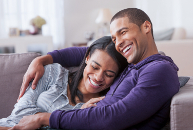 A man and woman smile and hug while sitting next to each other on a couch