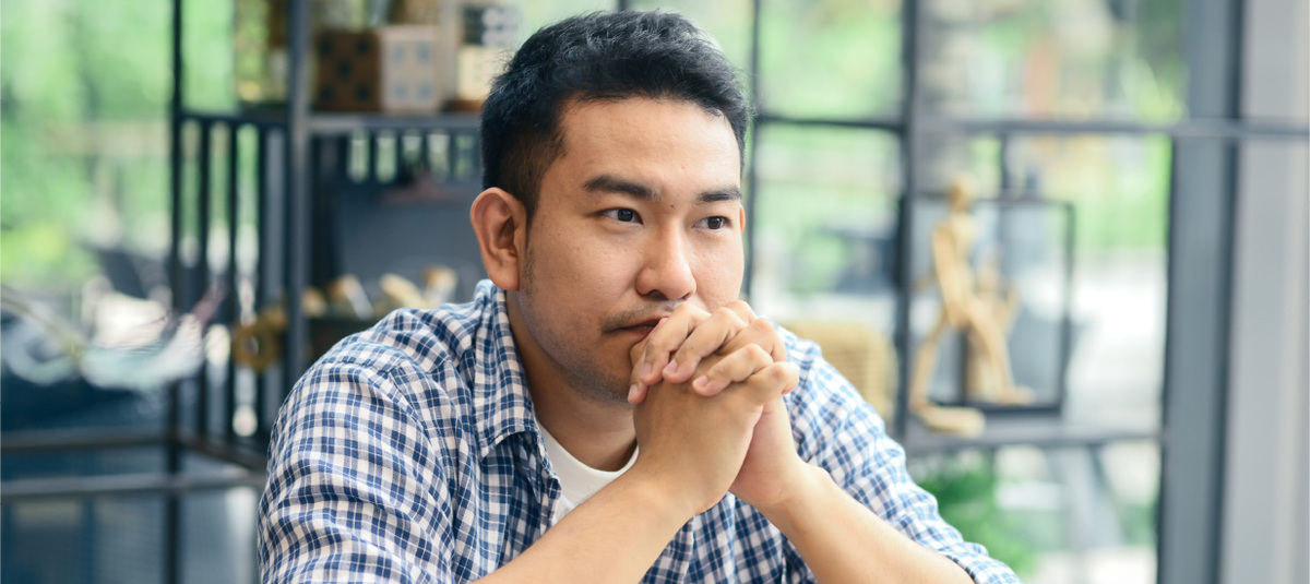 A man sits with his hands clasped in front of his face, thinking about how to manage his difficult emotions.