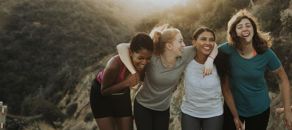 Four young women embrace on top of a mountain after a hike, building resilience and friendship through activity outdoors.