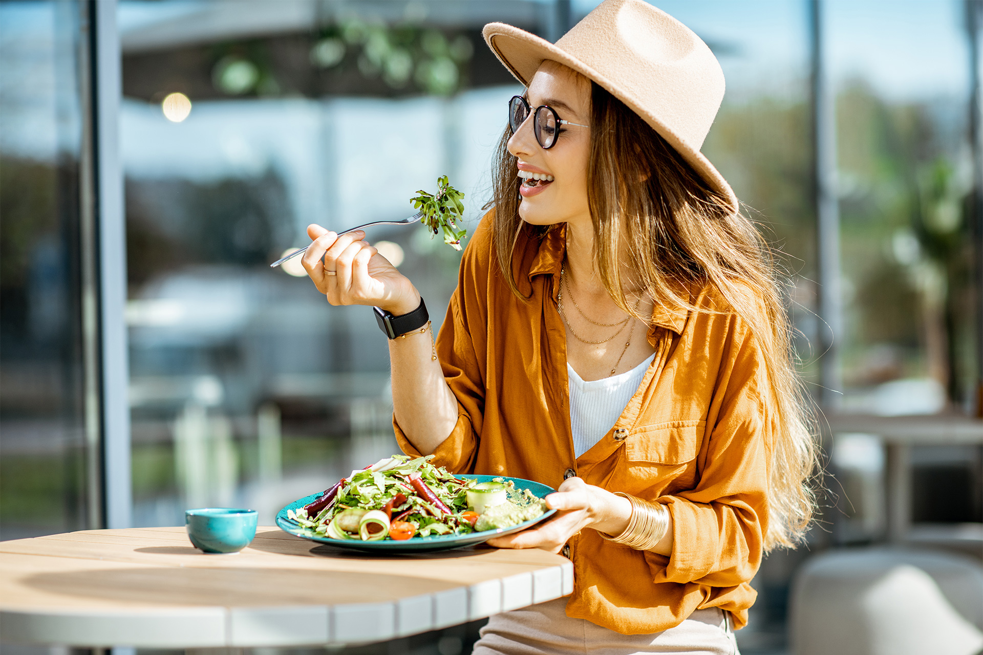 White woman with long blonde hair eating a salad outside in the sun