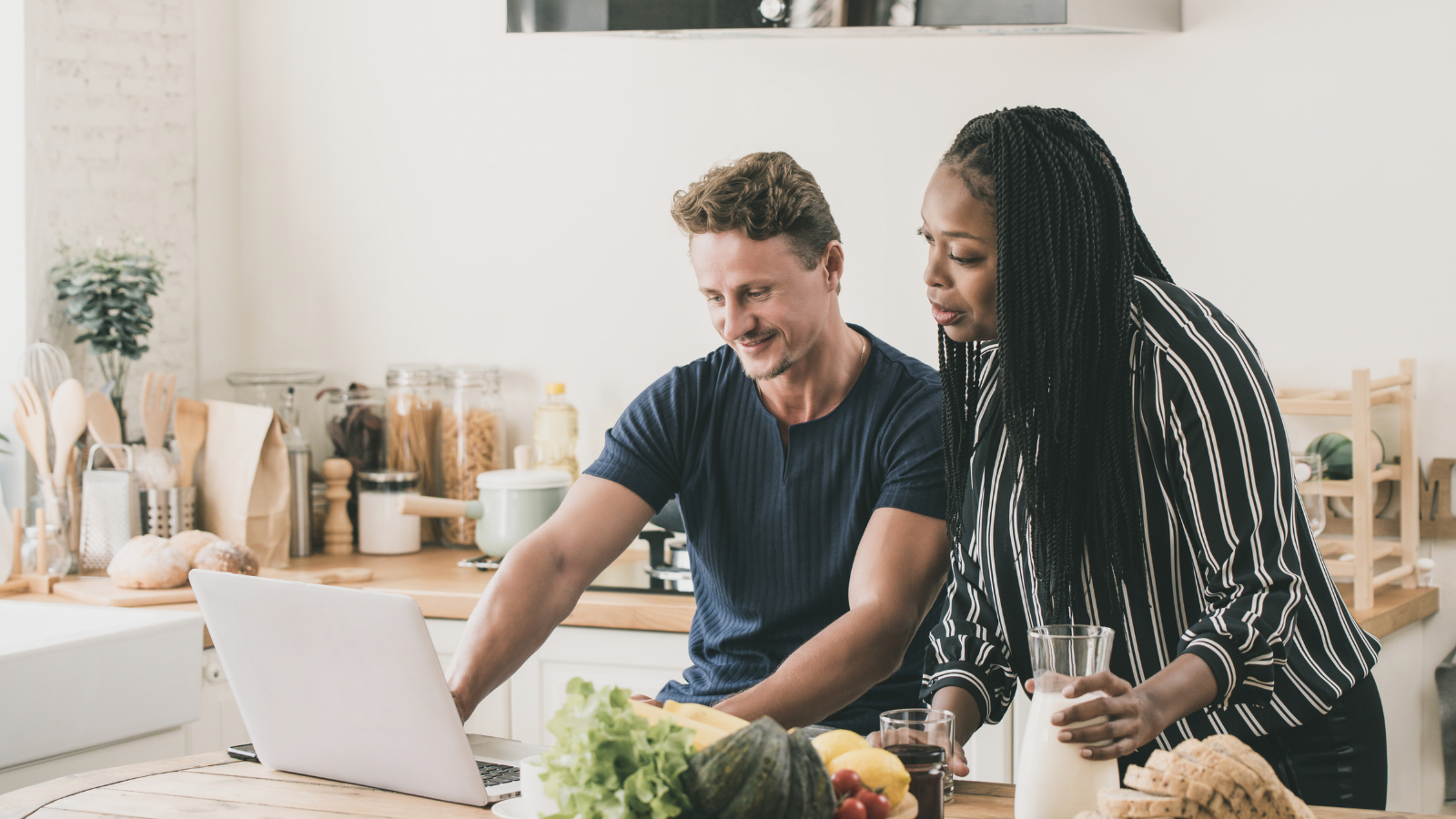 An interracial couple learns about diversity in relationships by watching LifeSpeak videos on their laptop in their kitchen.
