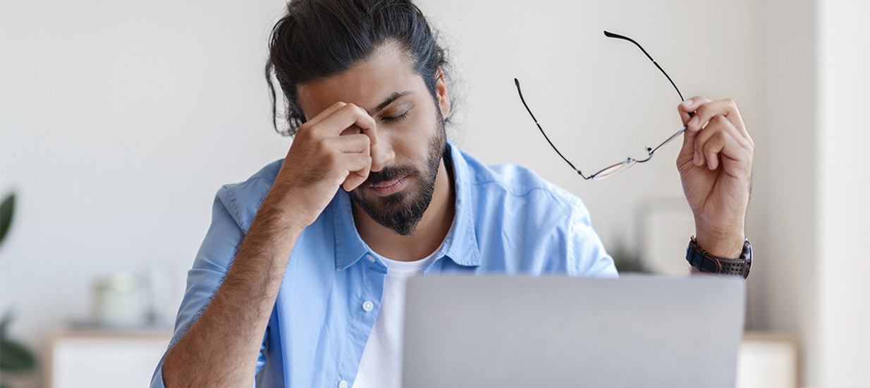 A stressed and hunched over person with their hand on the bridge of their nose, and their glasses in their other hand