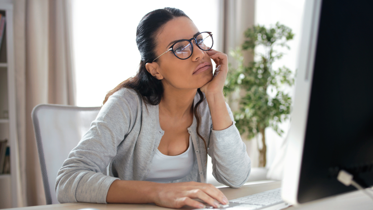 A young woman sitting at her desk, staring listlessly at her computer.