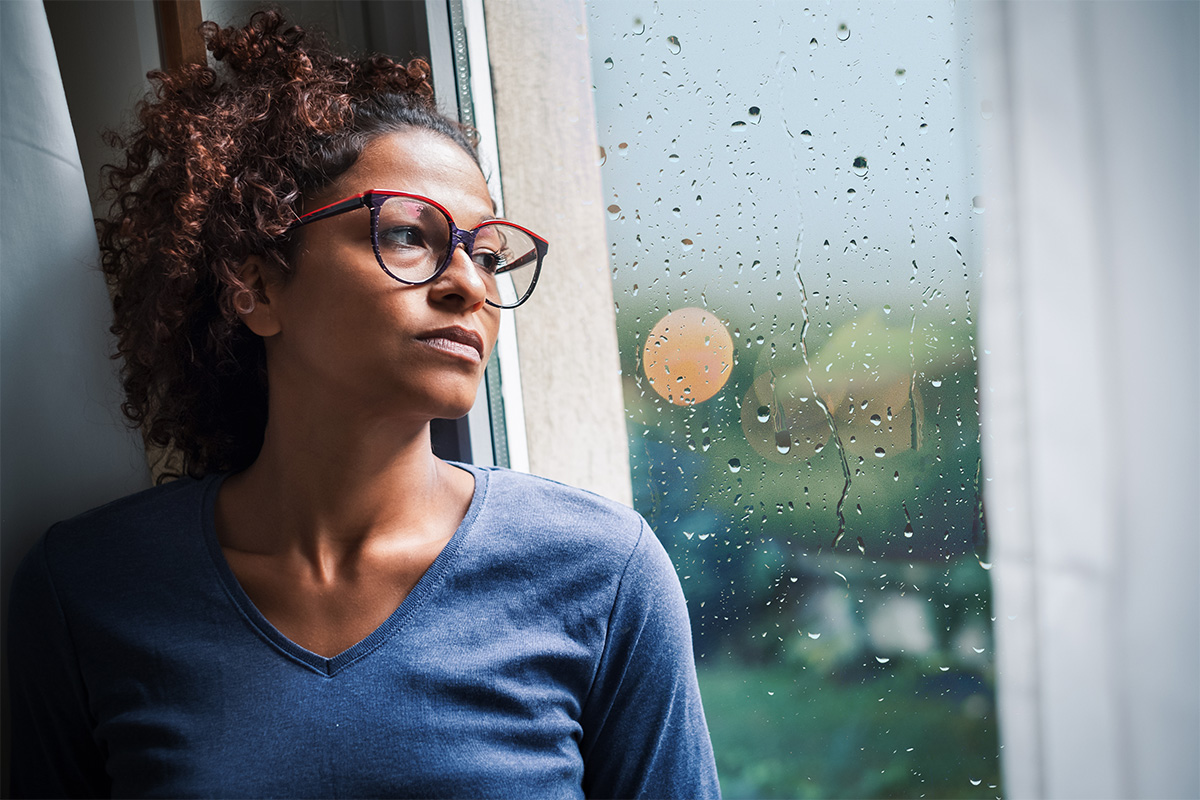 A woman grapples with her loneliness, staring out a window on a rainy day.