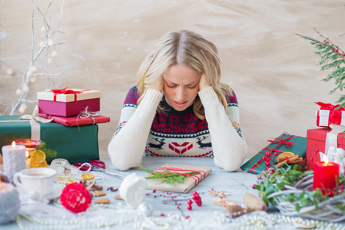 A female employee overcome with holiday stress holds her head in frustration while wrapping holiday gifts.
