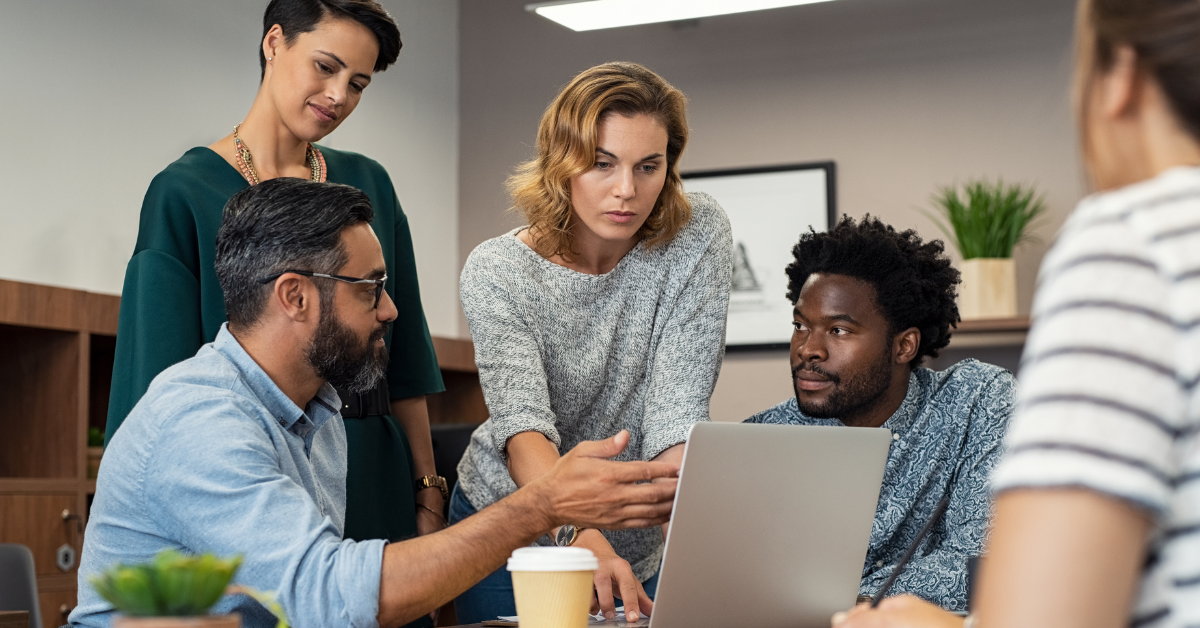 A group of five diverse employees are working around a laptop.