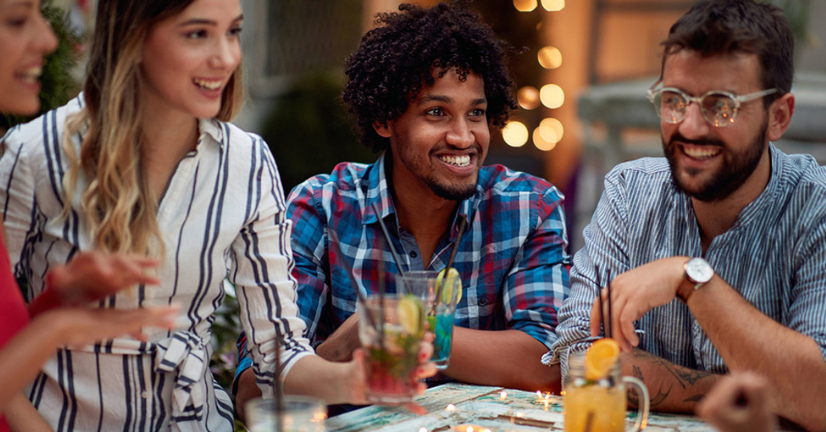 A group of diverse friends sitting around a table drinking.