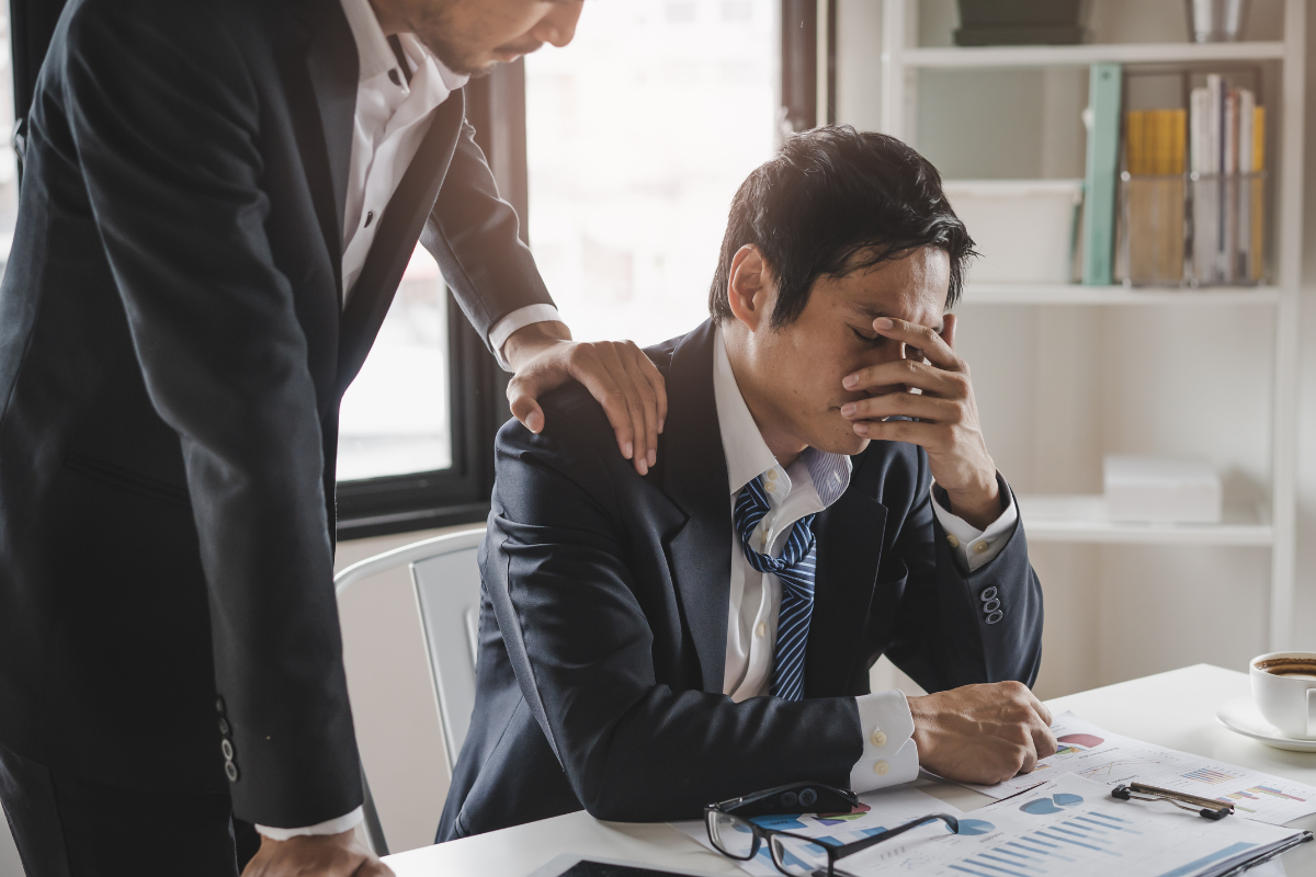 A manager supports an employee with a hand on the shoulder during a stressful time at work.