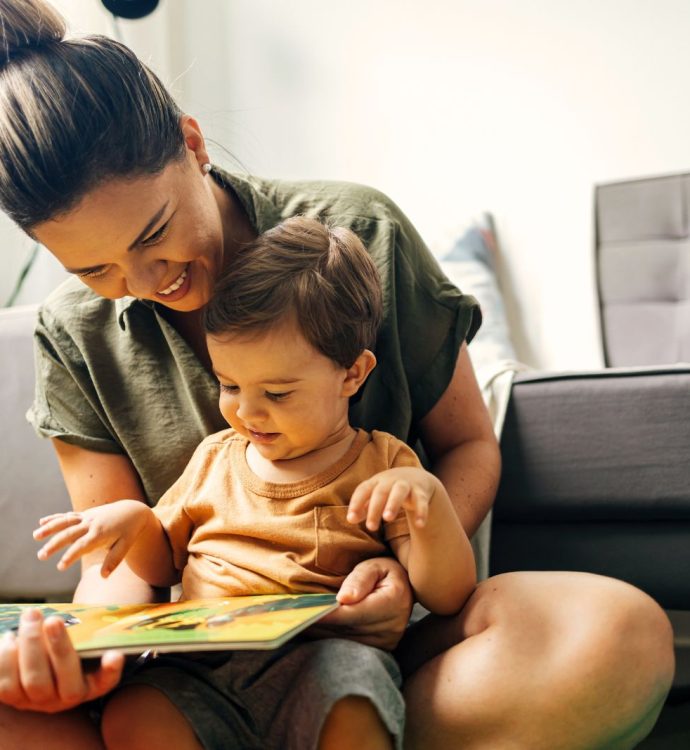 Parent reading a picture book to a child on the floor, smiling and engaged in a cozy room.