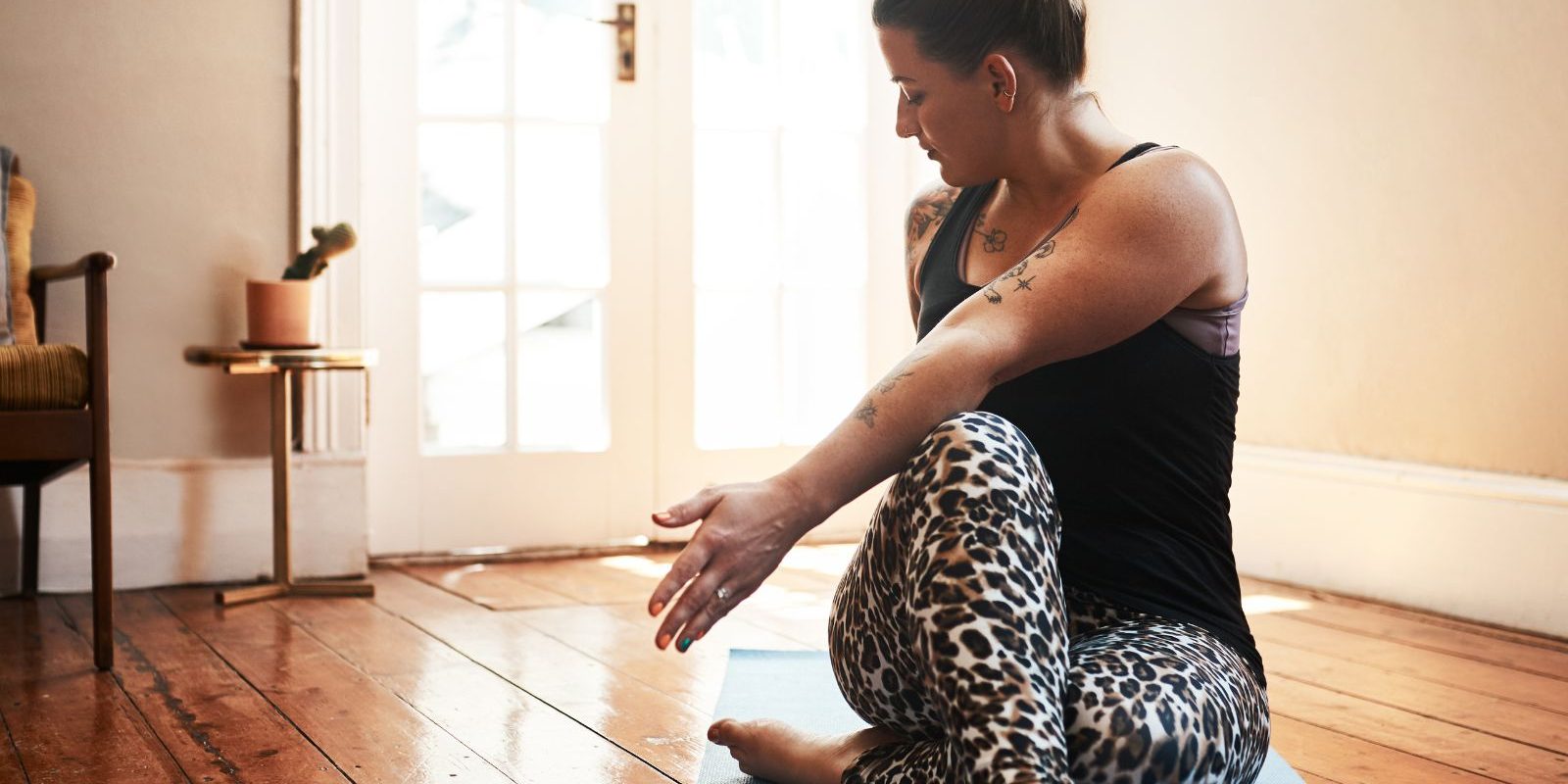 Woman in leopard leggings doing yoga twist pose on mat indoors.