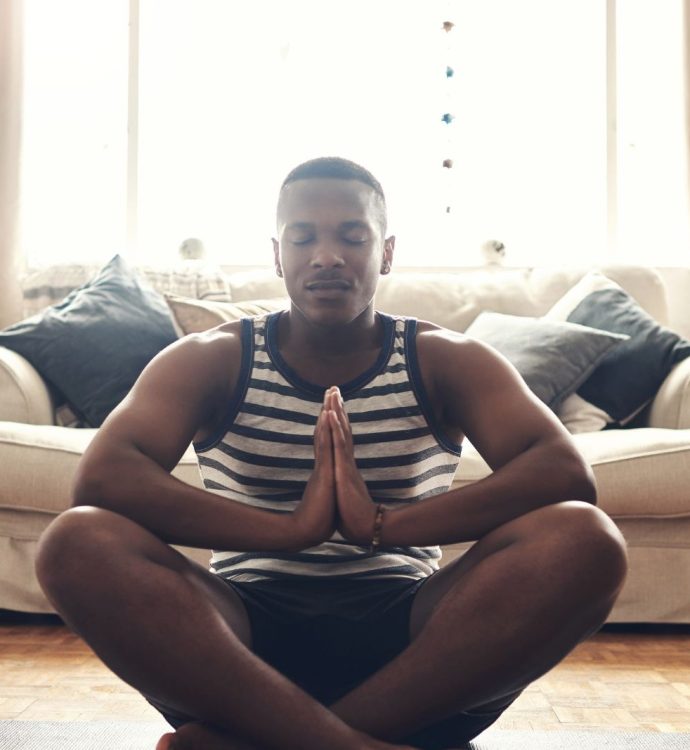 Man meditating at home, seated cross-legged in living room, practicing mindfulness.