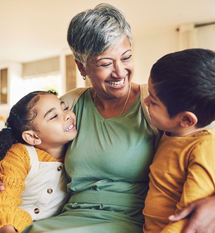 Smiling grandmother hugging two children on a cozy sofa at home.