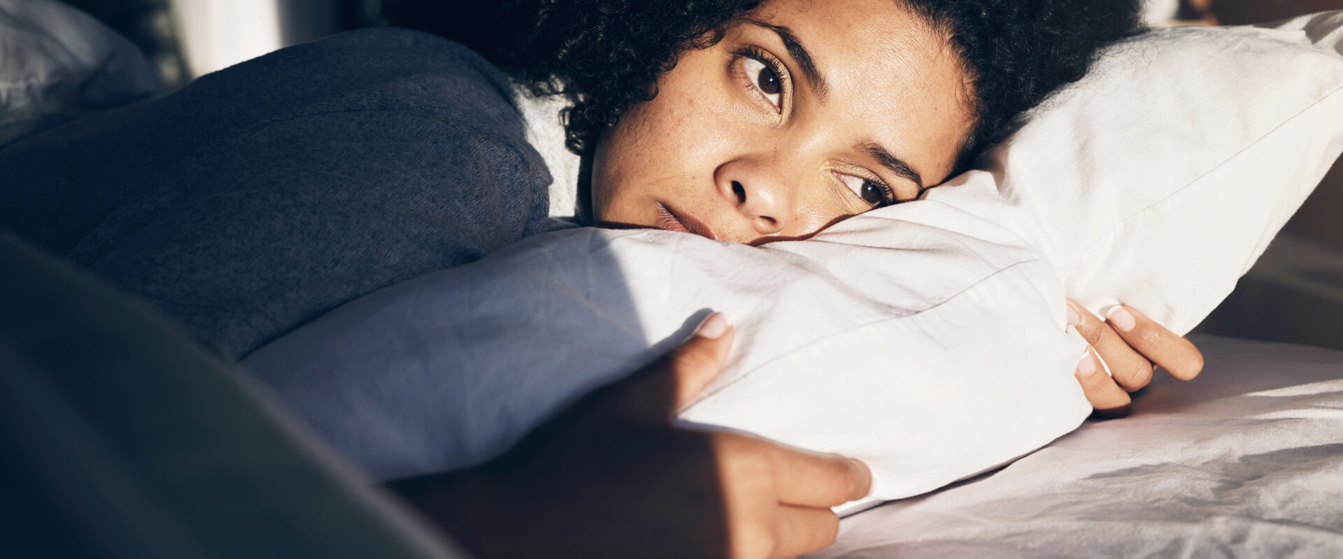 Woman deep in thought lying on a pillow, gazing out in sunlight.