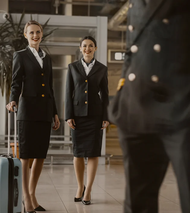 Airline crew in uniform with luggage at airport terminal.