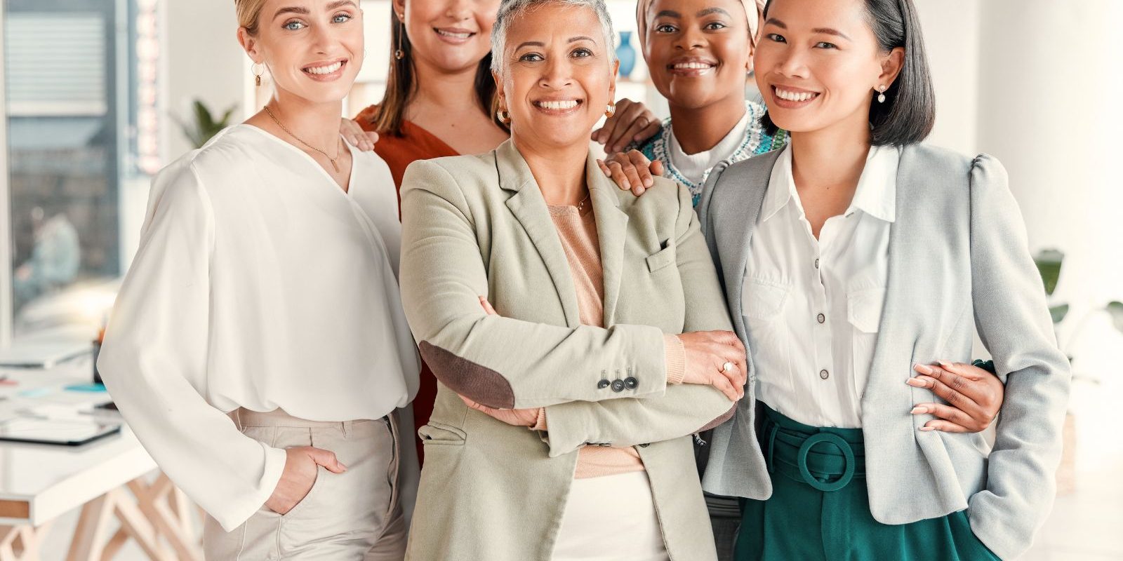 Diverse group of professional women smiling confidently in a bright office setting.