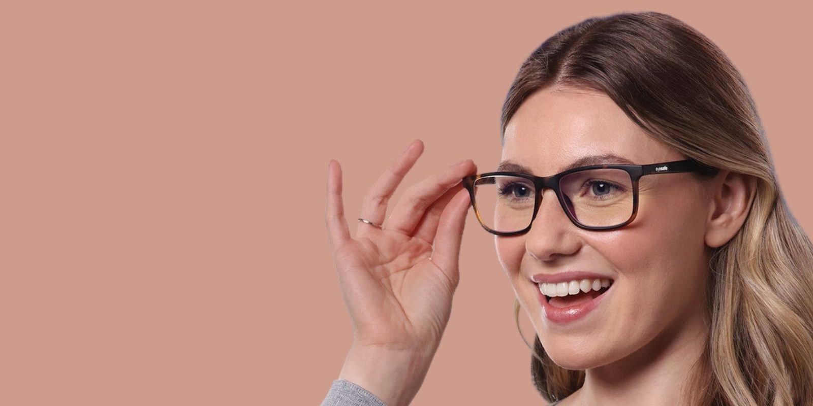 Smiling woman with glasses, touching frames, peach background.