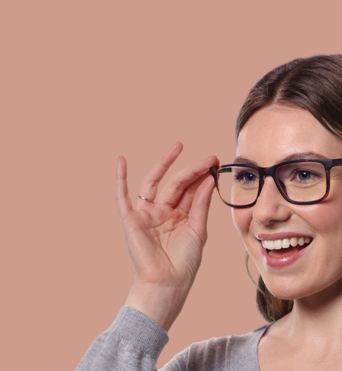 Smiling woman with glasses, touching frames, peach background.