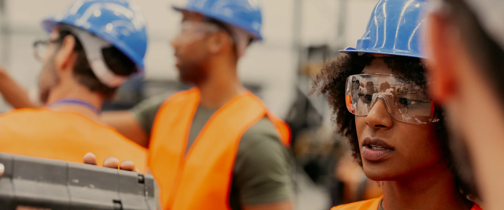 Workers in blue helmets and orange vests engaged in a discussion at a construction site.