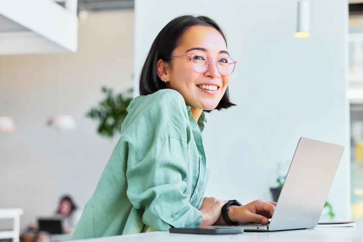 Young professional smiling while working on a laptop, representing a positive employee experience with a workplace wellness program