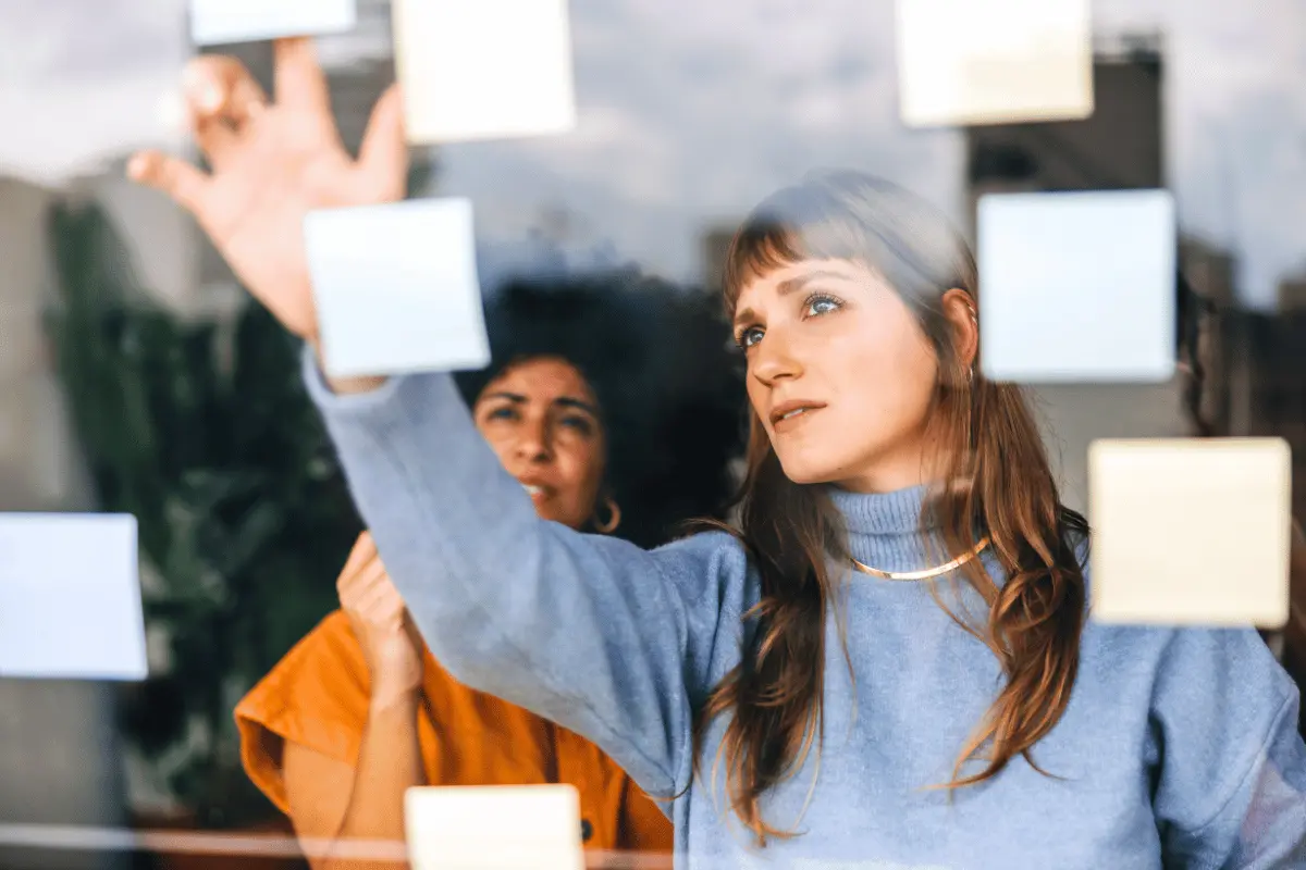 Two employees collaborating with sticky notes on a glass wall, feature image for Forbes article with LifeSpeak Founder Michael Held on questions HR leaders should ask about rising healthcare claims