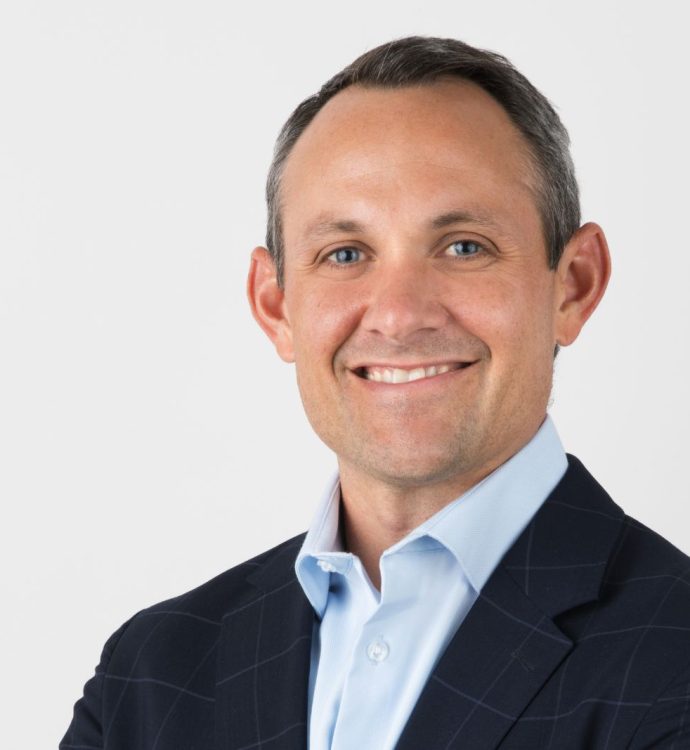 Smiling man in a suit with a light blue shirt, against a white background.