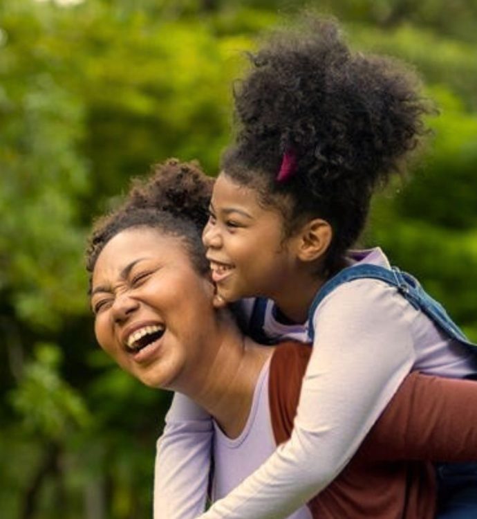 Mother and daughter enjoying a playful piggyback ride in a lush green park.