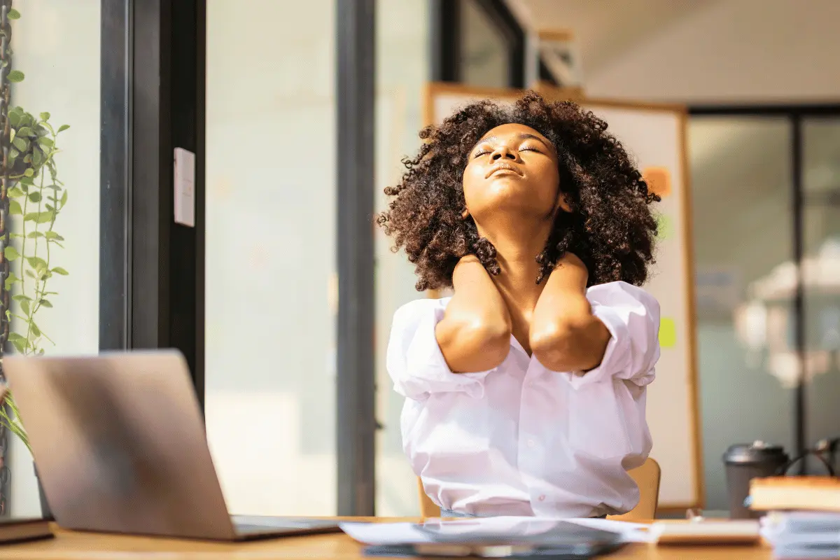 A woman at her desk holding her neck in discomfort, illustrating back and musculoskeletal pain at work.