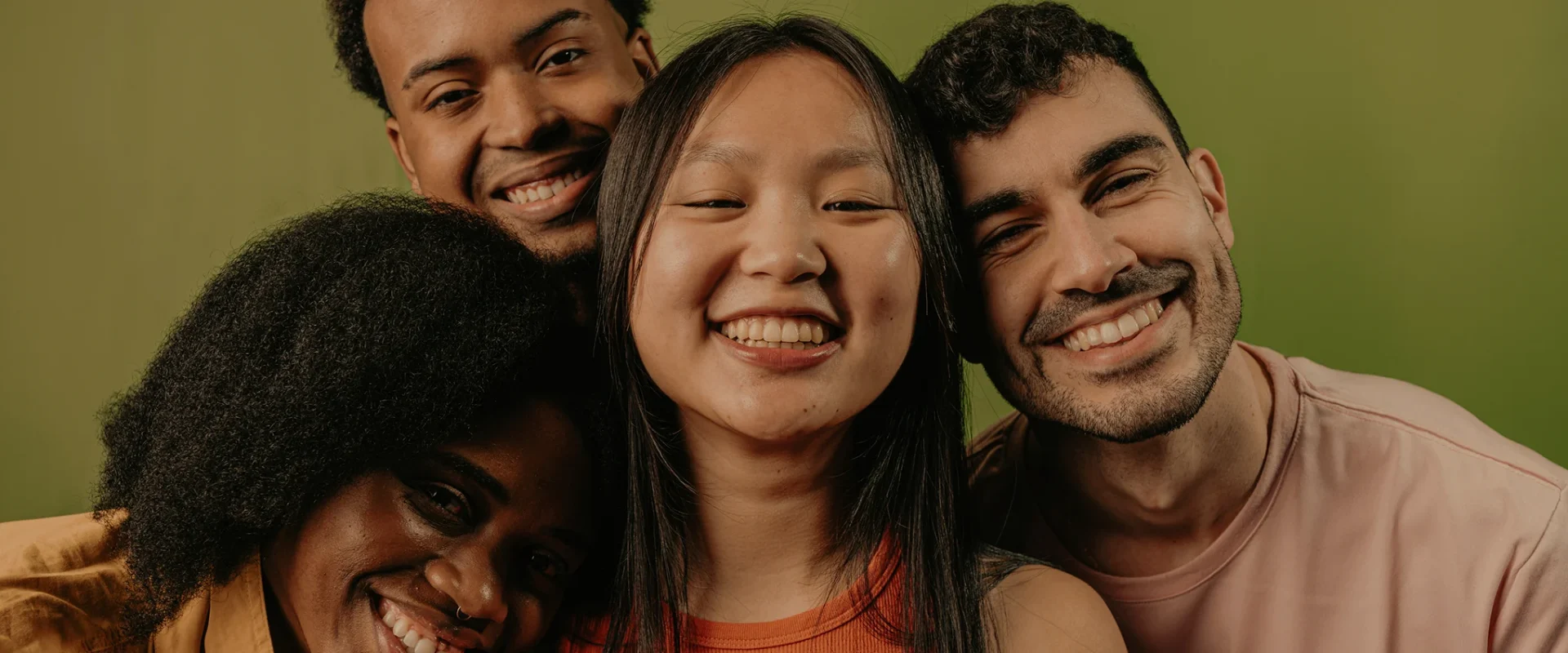 Group of friends smiling together against a green backdrop.