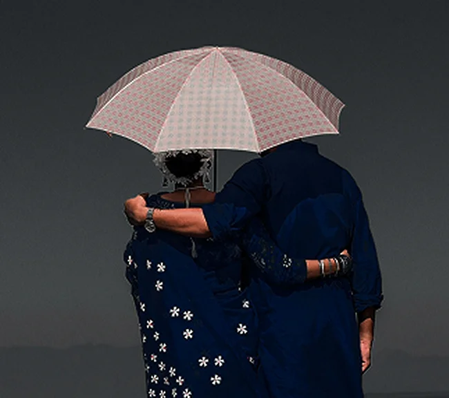 Couple under an umbrella, wearing dark clothing with floral patterns, embracing affectionately.