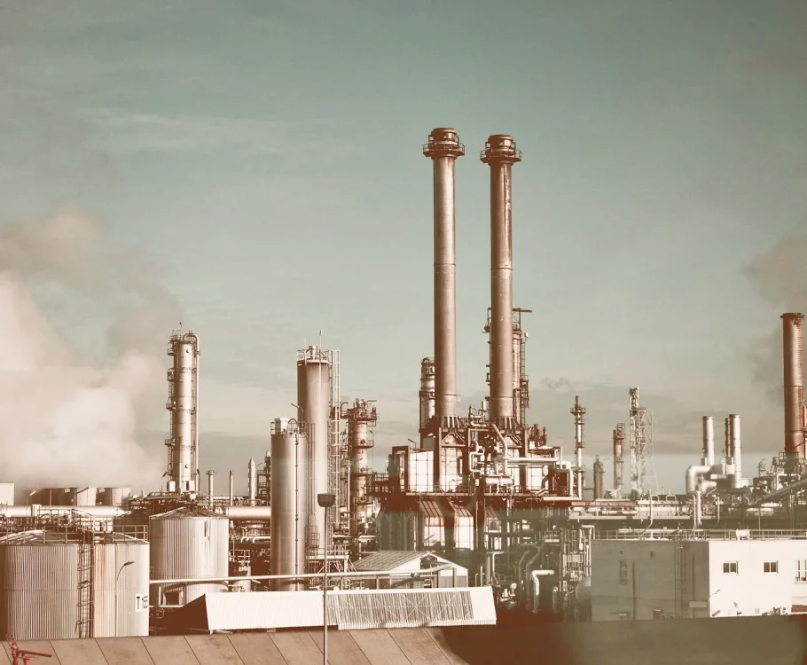 Industrial refinery with smokestacks and storage tanks under a clear sky.