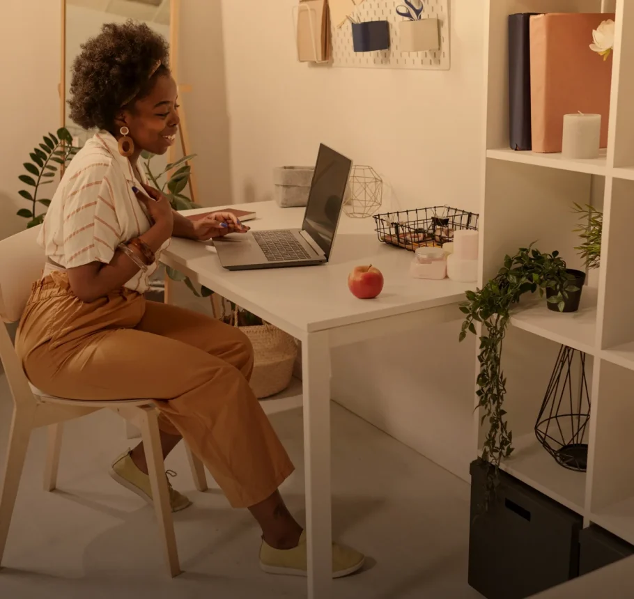 Woman working on a laptop at a home office desk with plants and decor.