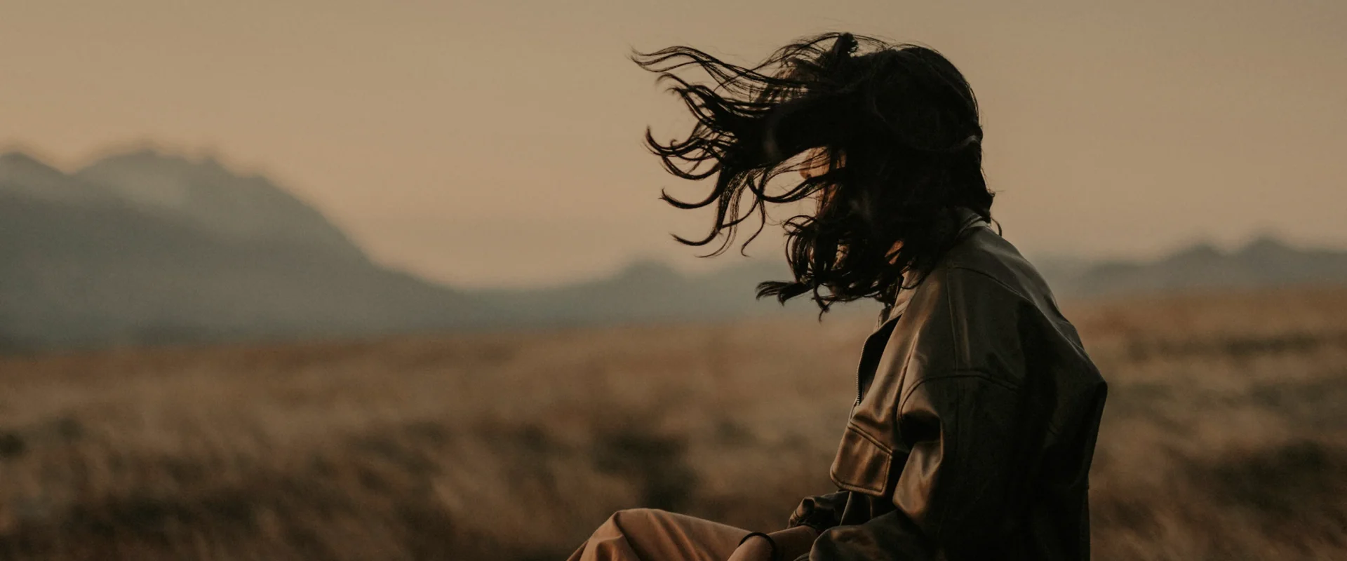 Woman with windblown hair in a field at sunset.