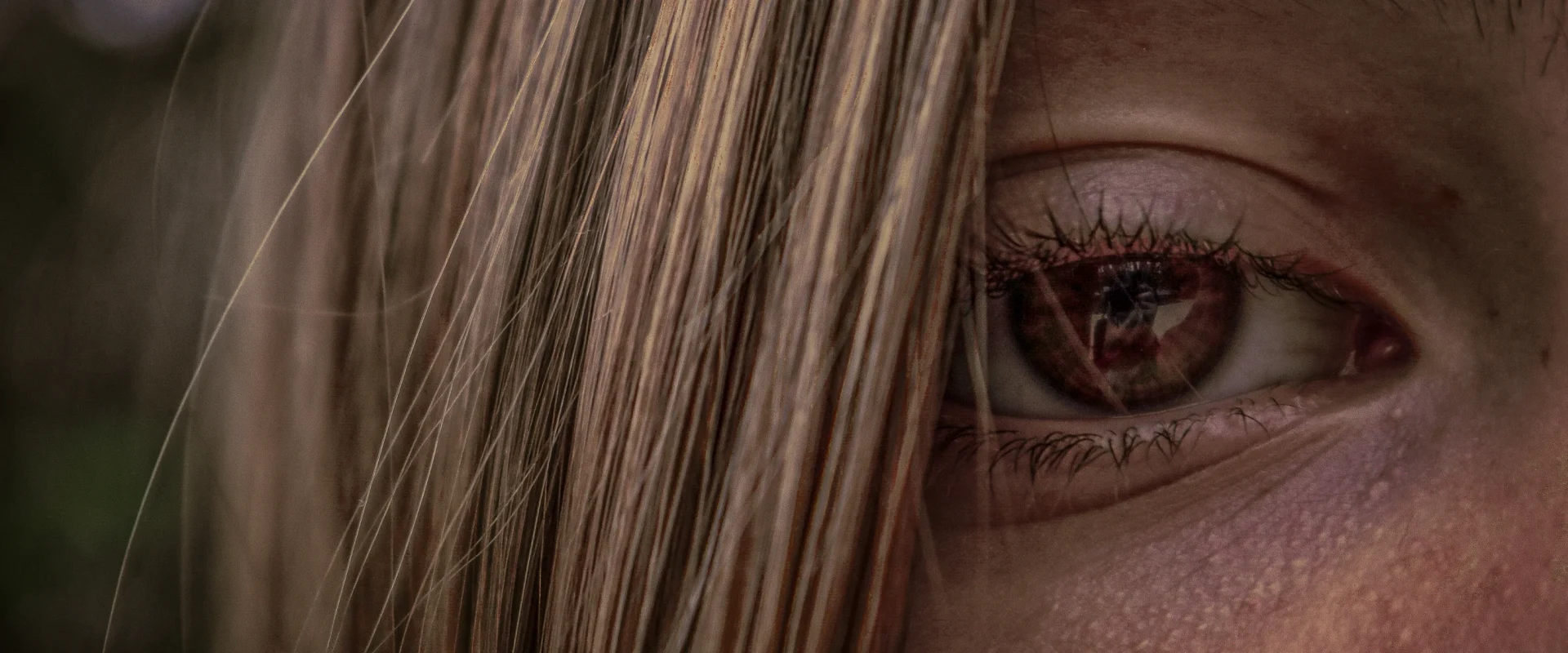 Close-up of a person's eye with hair partially covering the face, reflecting a detailed image.