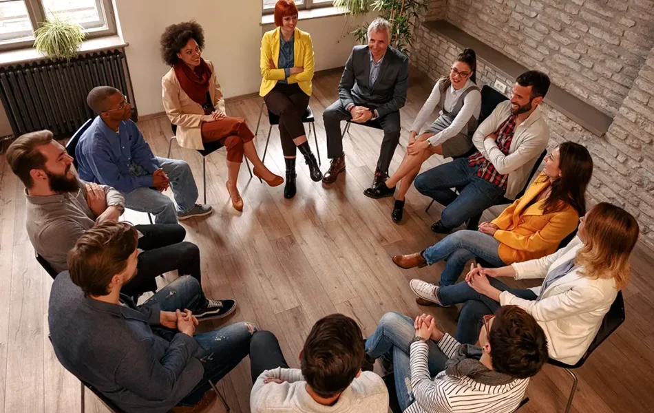 Group discussion in a circle in a bright room with diverse individuals seated on chairs.