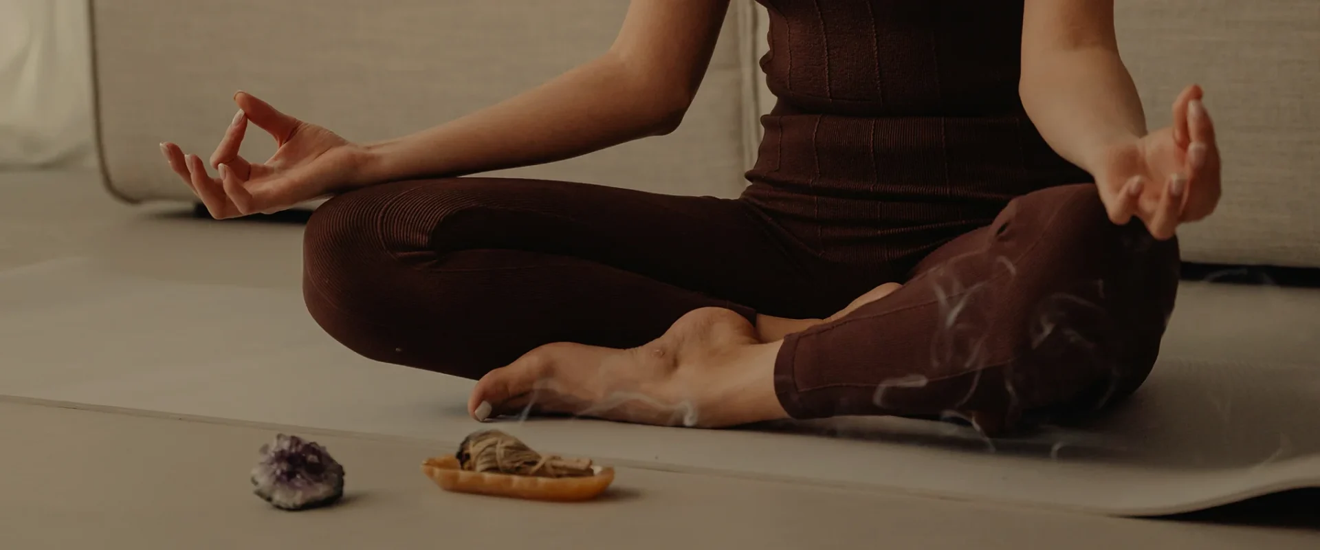 Person meditating in lotus pose with incense and crystals nearby. Relaxation and mindfulness.