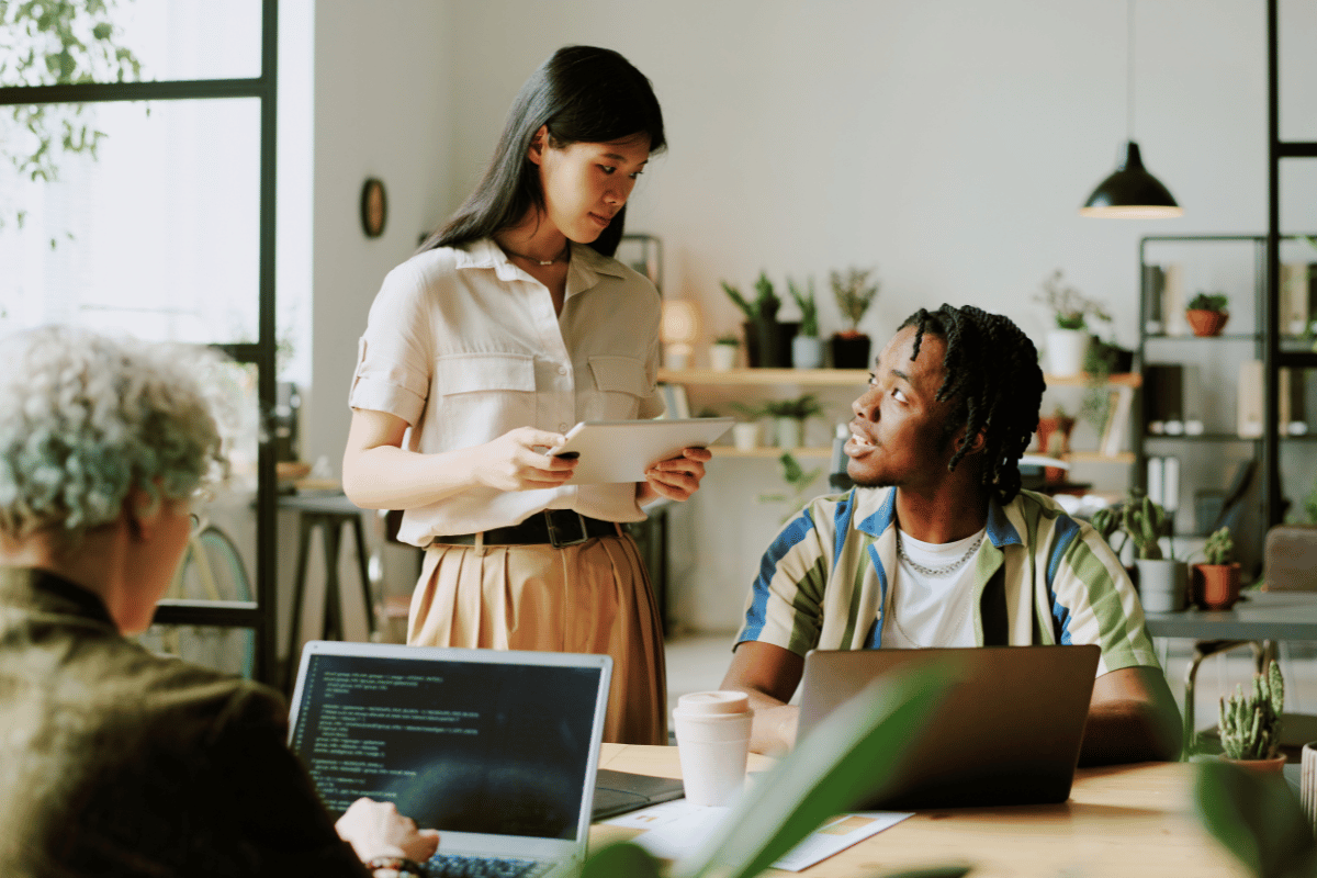 Two young professionals in a modern office discussing work around laptops, representing Gen Z employees and empathy-driven collaboration at work