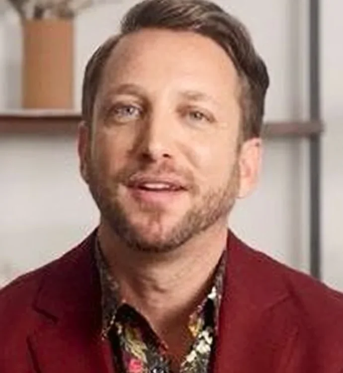 Man in a red jacket with patterned shirt, smiling indoors.