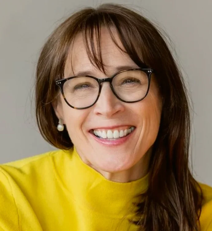 Smiling woman in glasses and yellow sweater, happy expression.