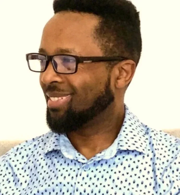 Smiling man in glasses and patterned shirt looking to the side.