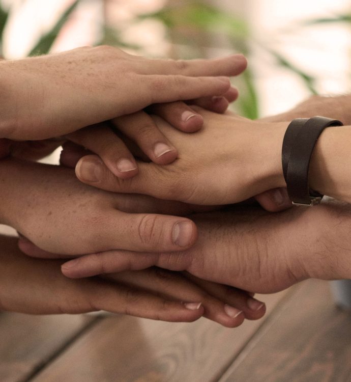 Hands joined together symbolizing teamwork and unity on a wooden table.