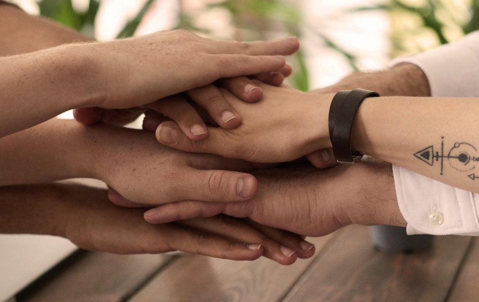 Hands joined together symbolizing teamwork and unity on a wooden table.