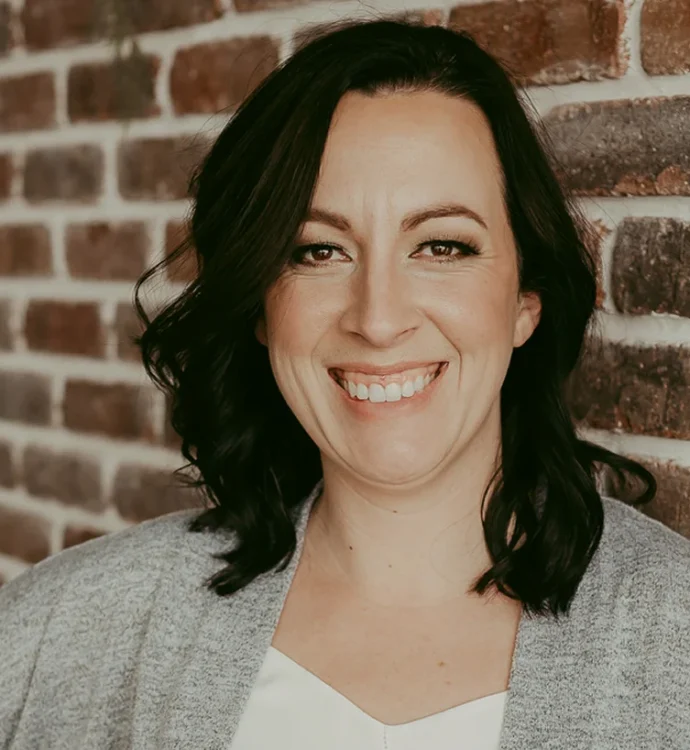 Smiling woman in gray sweater against a brick wall backdrop.