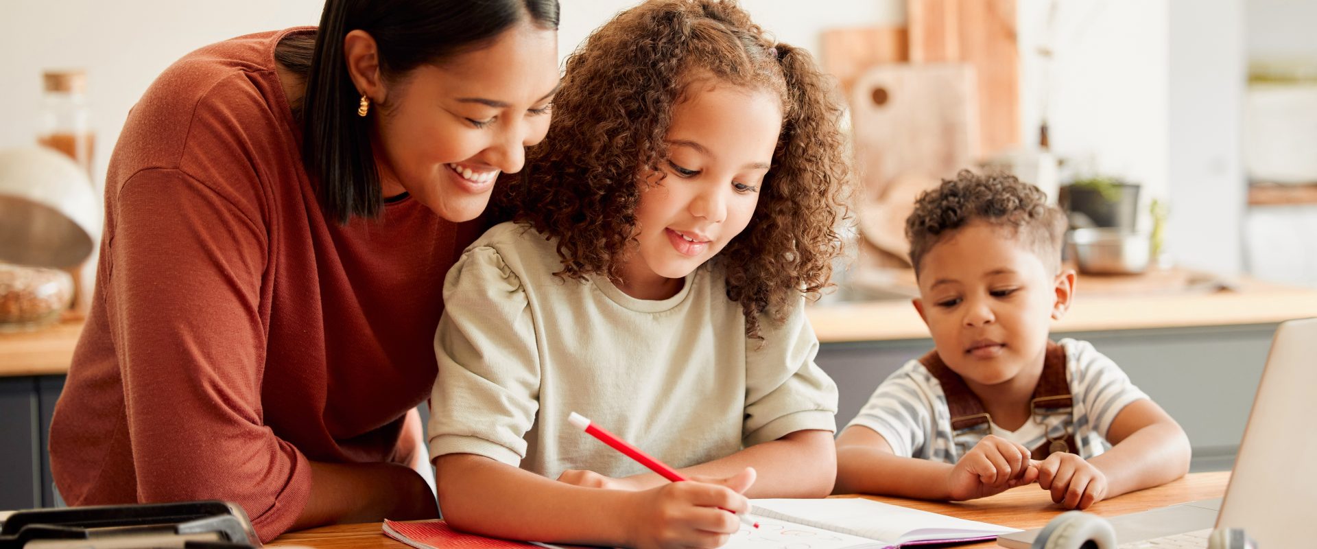 A mother helping her children with homework at the kitchen table, smiling and engaged.