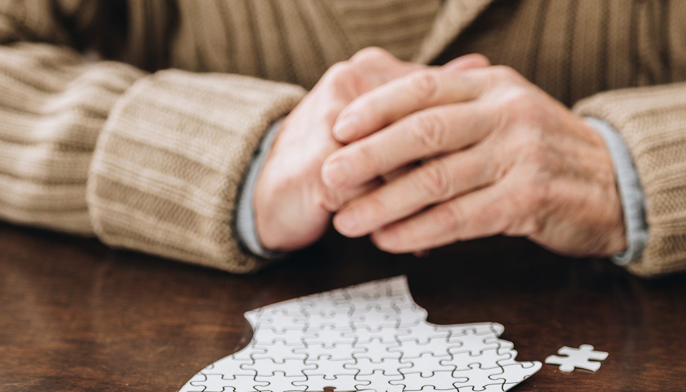 Elderly person with puzzle, symbolizing memory and mental health, at a table.