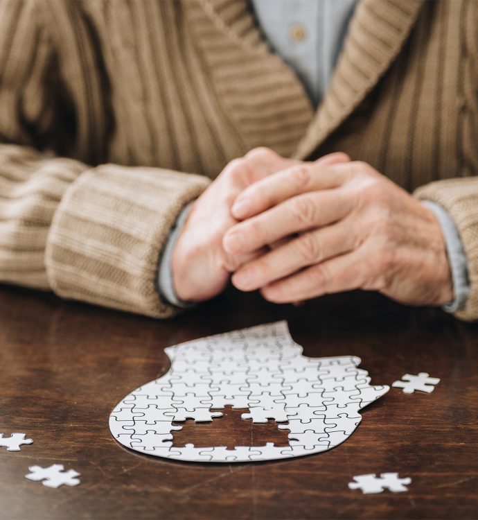 Elderly person with puzzle, symbolizing memory and mental health, at a table.