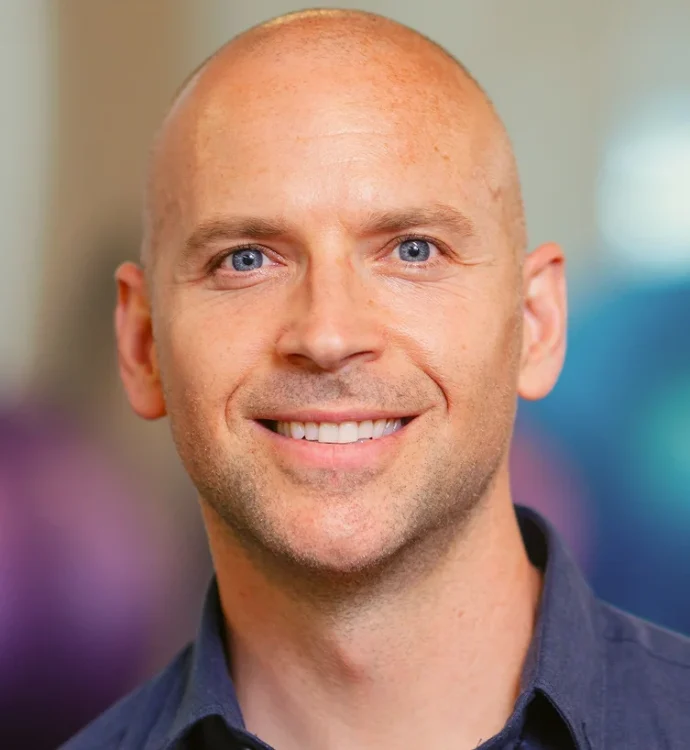 Smiling bald man with blue eyes wearing a dark shirt, professional headshot indoors
