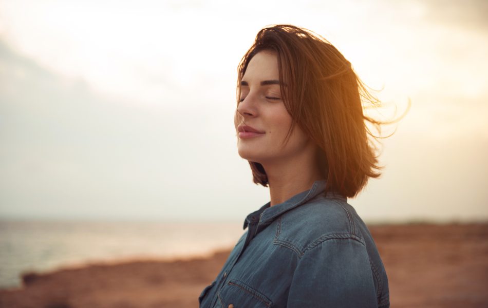 Woman enjoying seaside sunset with eyes closed, feeling relaxed and peaceful.