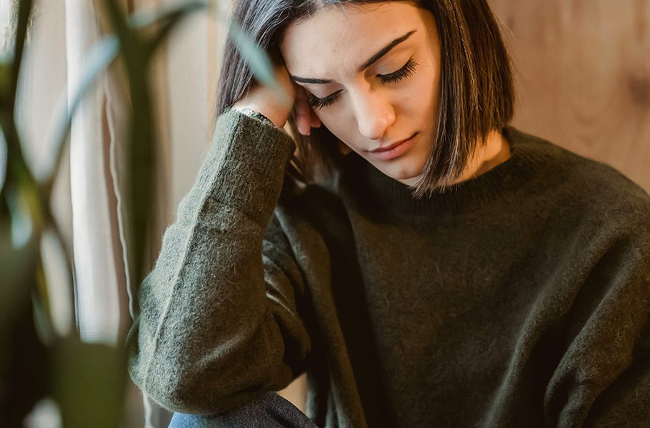 Woman in green sweater sitting indoors, looking down thoughtfully.